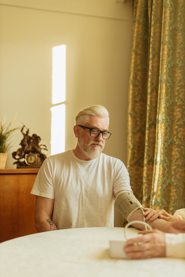 Senior man in eyeglasses checks blood pressure in a well-lit room.